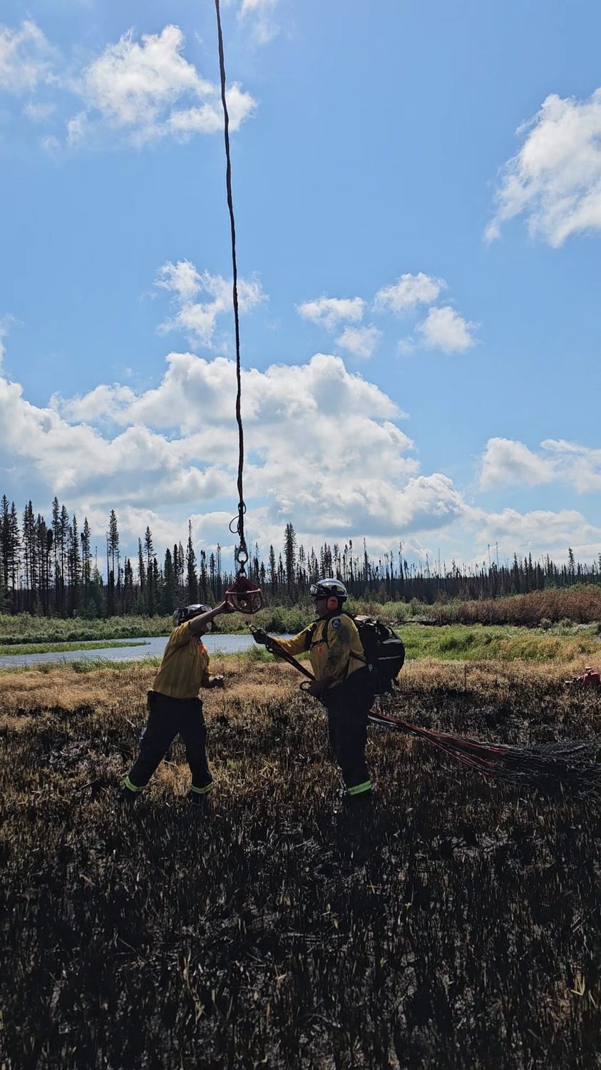 Australian wildland firefighters guiding suspended equipment in a burned field with Mystery Ranch packs.